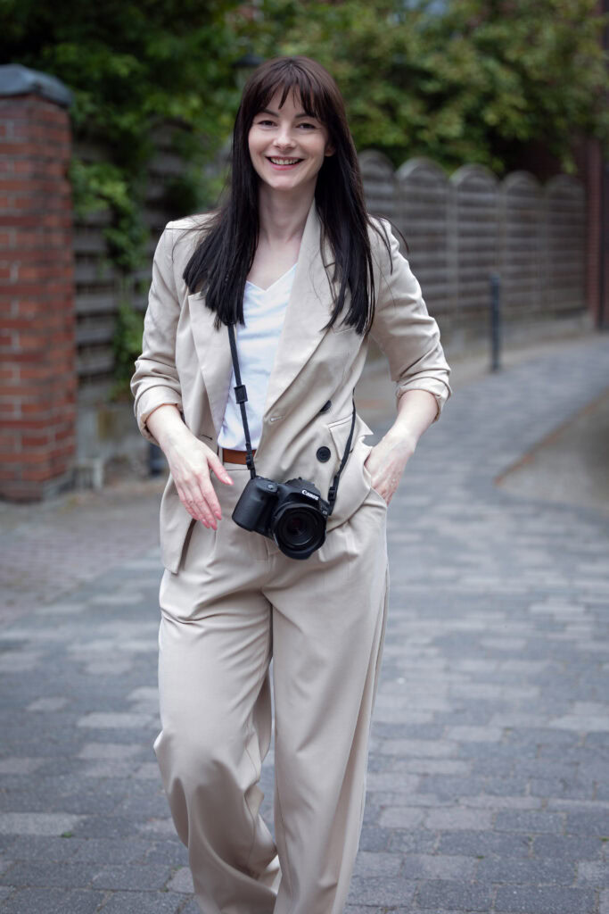 Fotografin mit Kamera in der Hand, lächelnd auf einer Straße in Münster - professionelles Branding-Shooting